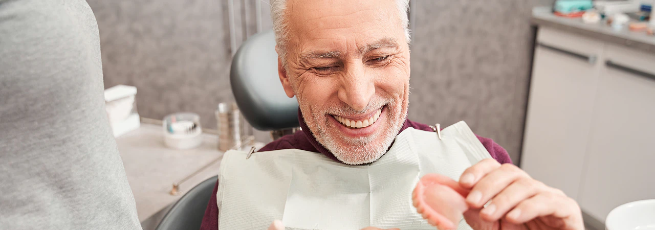 Smiling senior patient holding his denture in the dental chair